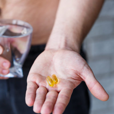 A Young Man Holds Vitamins And A Glass Of Water In His Hands. Immunity Pills
