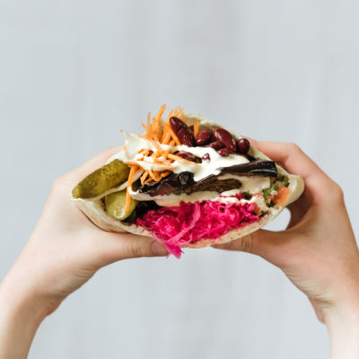 Closeup Shot Of Hands Holding Vegetarian Shawarma With Red Beans, And Pickles Wrapped In Pita Bread